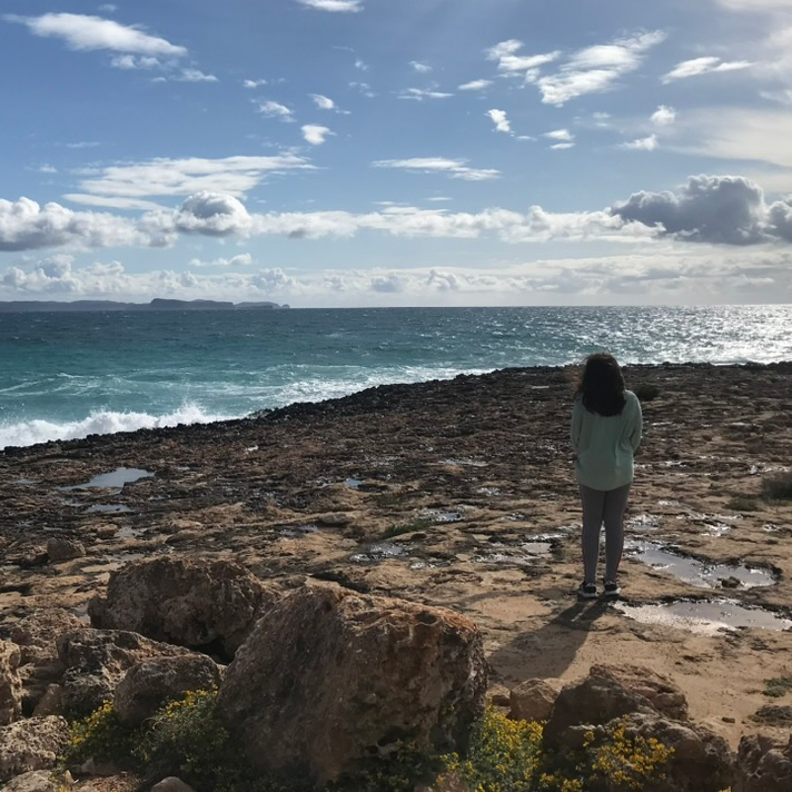 Eine Frau steht an einem steinigen Strand am Meer